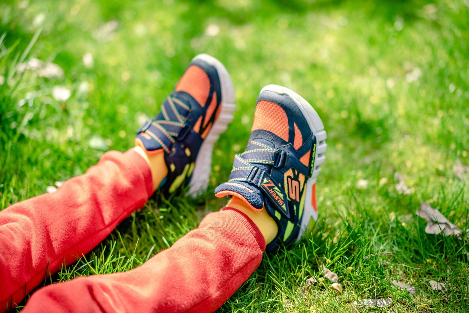 A close-up shot of a child's colorful sneakers on vibrant green grass under daylight.