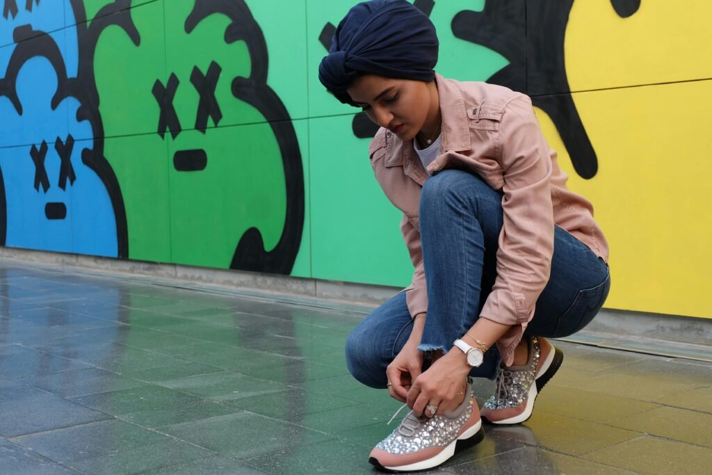 Fashionable woman adjusts shoelaces outdoors against vibrant mural background.