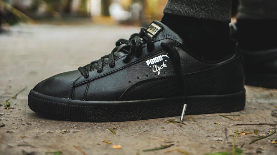 Close-up of black Puma Clyde sneaker on a textured outdoor surface, showcasing fashion and style.