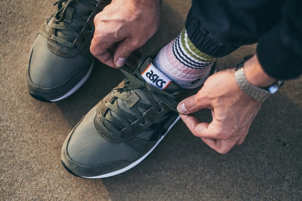 Close-up of a man tying shoelaces wearing green sneakers with striped socks outdoors.
