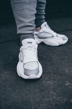 Detailed close-up of PUMA white sneakers on a textured asphalt surface, emphasizing modern footwear style.